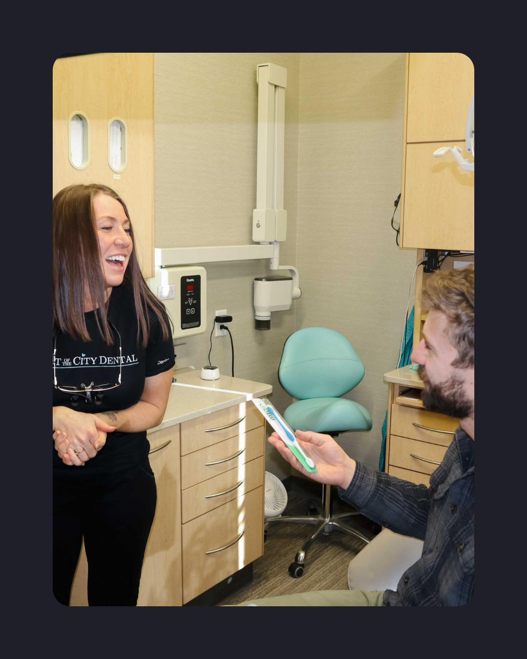 Dental team member speaking with a patient and handing them a toothbrush inside a dental exam room.